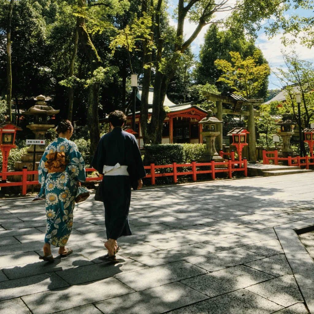 Pareja caminando con yukata por un santuario entre sombras de árboles.