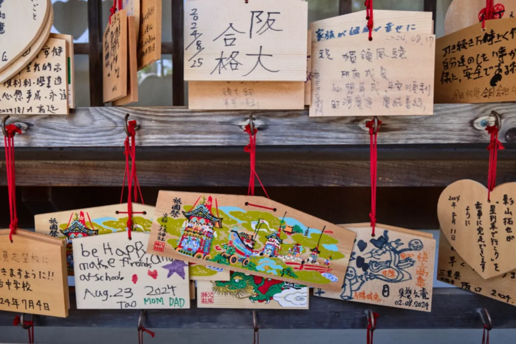 Tablillas ema de madera con deseos escritos, cuelgan con cuerdas rojas en un templo japonés, tradición popular entre familias y viajeros.