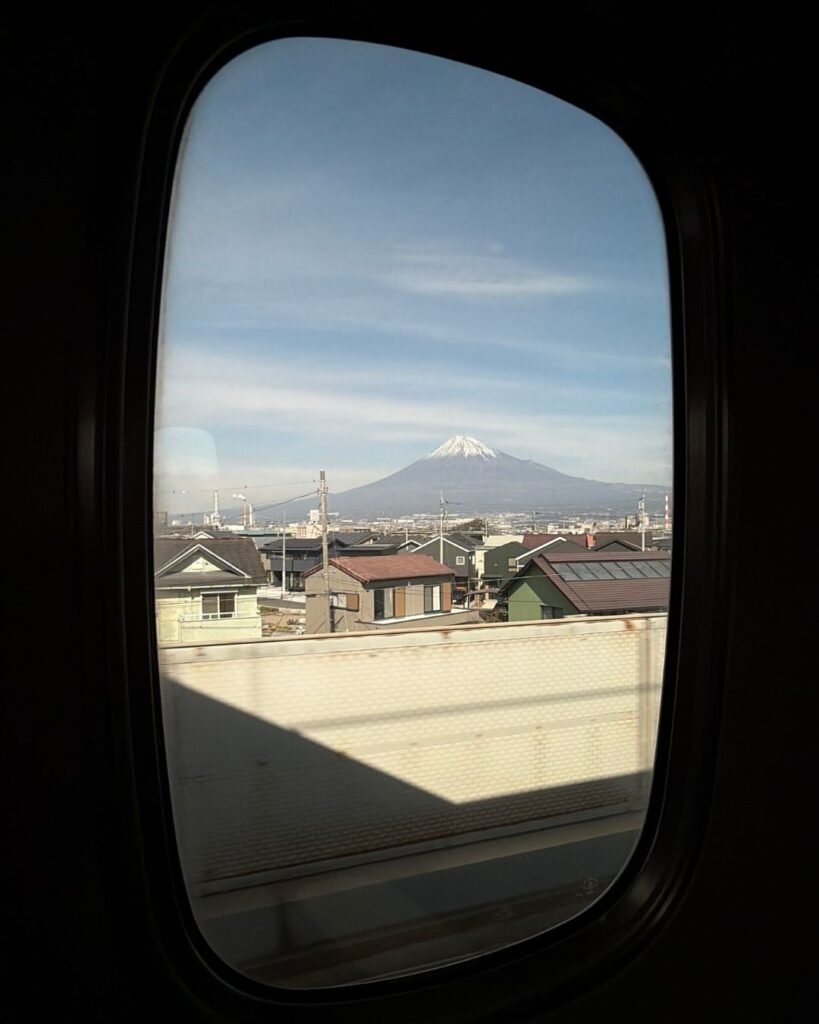El Monte Fuji nevado sobre la ciudad visto a través de la ventanilla de un tren.